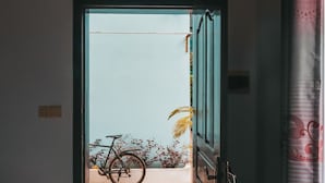 En døråbning der fører til en balkon med en cykel og planter.
