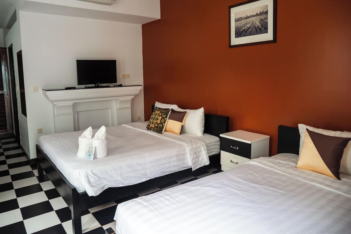 A hotel room with two beds, a television on a white console, and a framed picture on the wall.