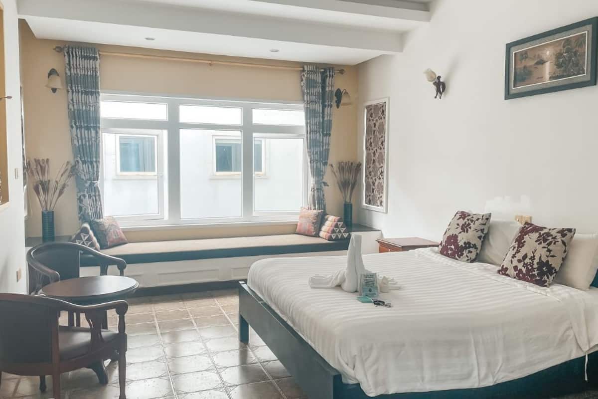 A bedroom with a bed, a chair, a table, and a window with curtains.
