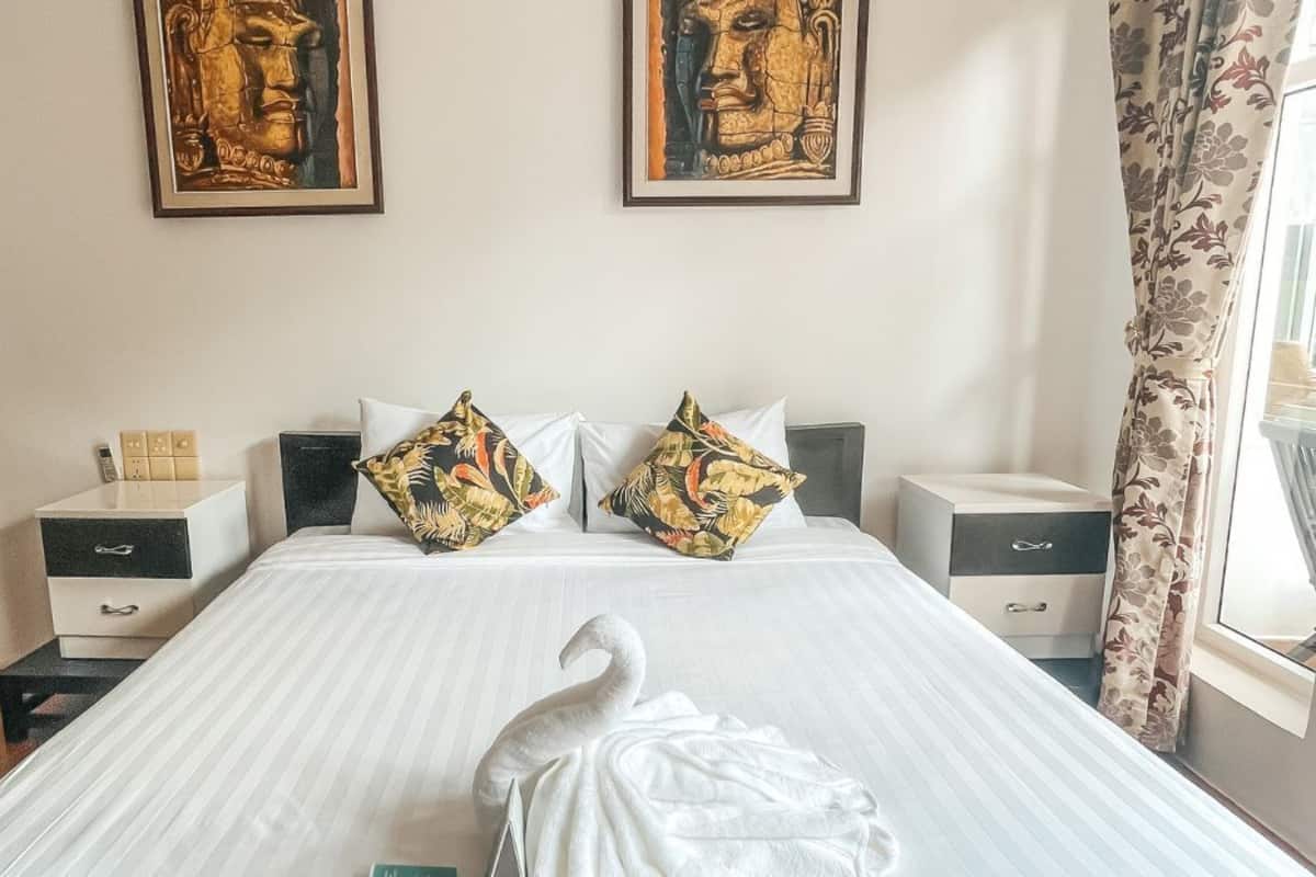 A hotel room with a large bed, two nightstands, a swan decoration, and two framed artworks on the wall.