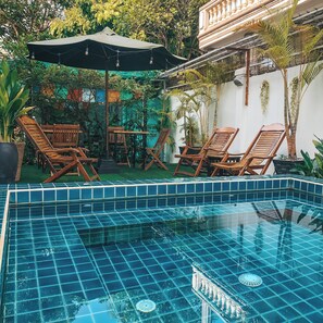 A swimming pool with blue tiles, surrounded by wooden lounge chairs and a table. - The Bygone (Siem Reap)