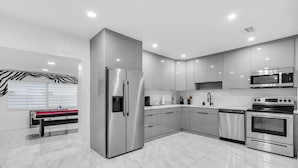 A modern kitchen with stainless steel appliances, white cabinetry, and a marble floor. - Miami Backyard Oasis • 4BR • Pool Table • Pergola • Spacious Outdoor Retreat (North Miami Beach)