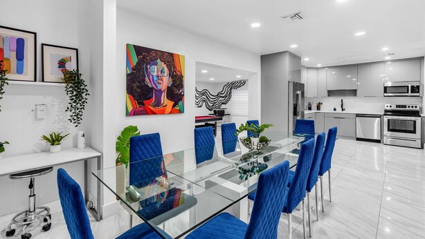 A modern kitchen with stainless steel appliances, a glass dining table with blue chairs, and a white countertop. - Miami Backyard Oasis • 4BR • Pool Table • Pergola • Spacious Outdoor Retreat (North Miami Beach)