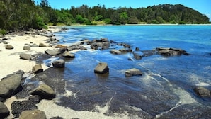 Una spiaggia con acque cristalline turchesi, rocce e un'isola verdeggiante sullo sfondo.