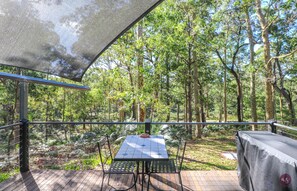 An outdoor deck with a table and chairs, surrounded by a forested area. - The Bower At Broulee (Broulee)
