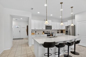 A modern kitchen with white cabinets, a large island with bar stools, stainless steel appliances, and pendant lighting.