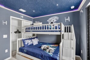 A room with a bunk bed, a ceiling with a starry design, and Star Wars-themed wall decals.