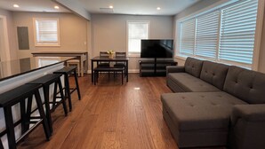 A modern living room with a dining area, a flat-screen TV, and large windows with blinds. - Cheerful 2 Home (Riviera Beach)