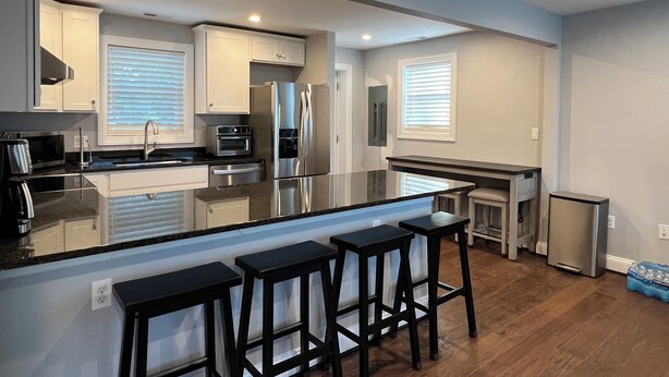A modern kitchen with a central island, bar stools, stainless steel appliances, and a small refrigerator. - Cheerful 2 Home (Riviera Beach)