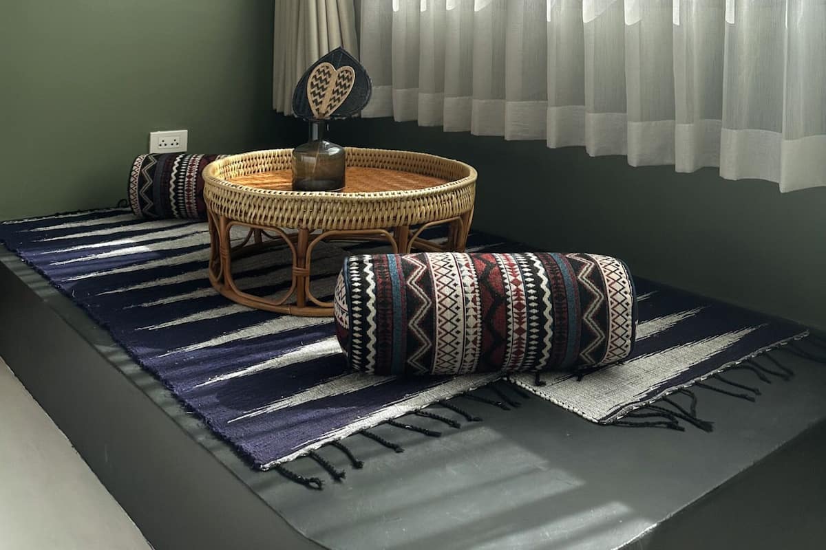A room with a green wall, a woven rattan chair, a round table, and a striped rug.