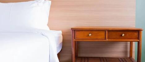 Un lit bien fait, avec du linge de lit blanc, une table de chevet en bois dotée de deux tiroirs et un luminaire fixé au mur.
