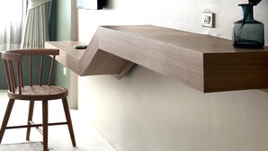 Una habitación moderna con escritorio integrado, una silla, un televisor, un espejo y una ventana con cortinas.