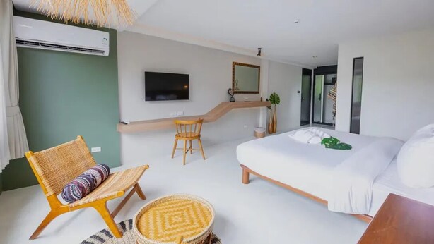 Un dormitorio moderno con cama, una silla, una mesita, televisión y espejo.
