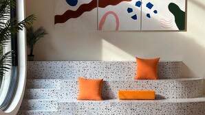 Una sala de estar moderna con un sofá, cojines naranja, un tapete estampado y arte abstracto en la pared.