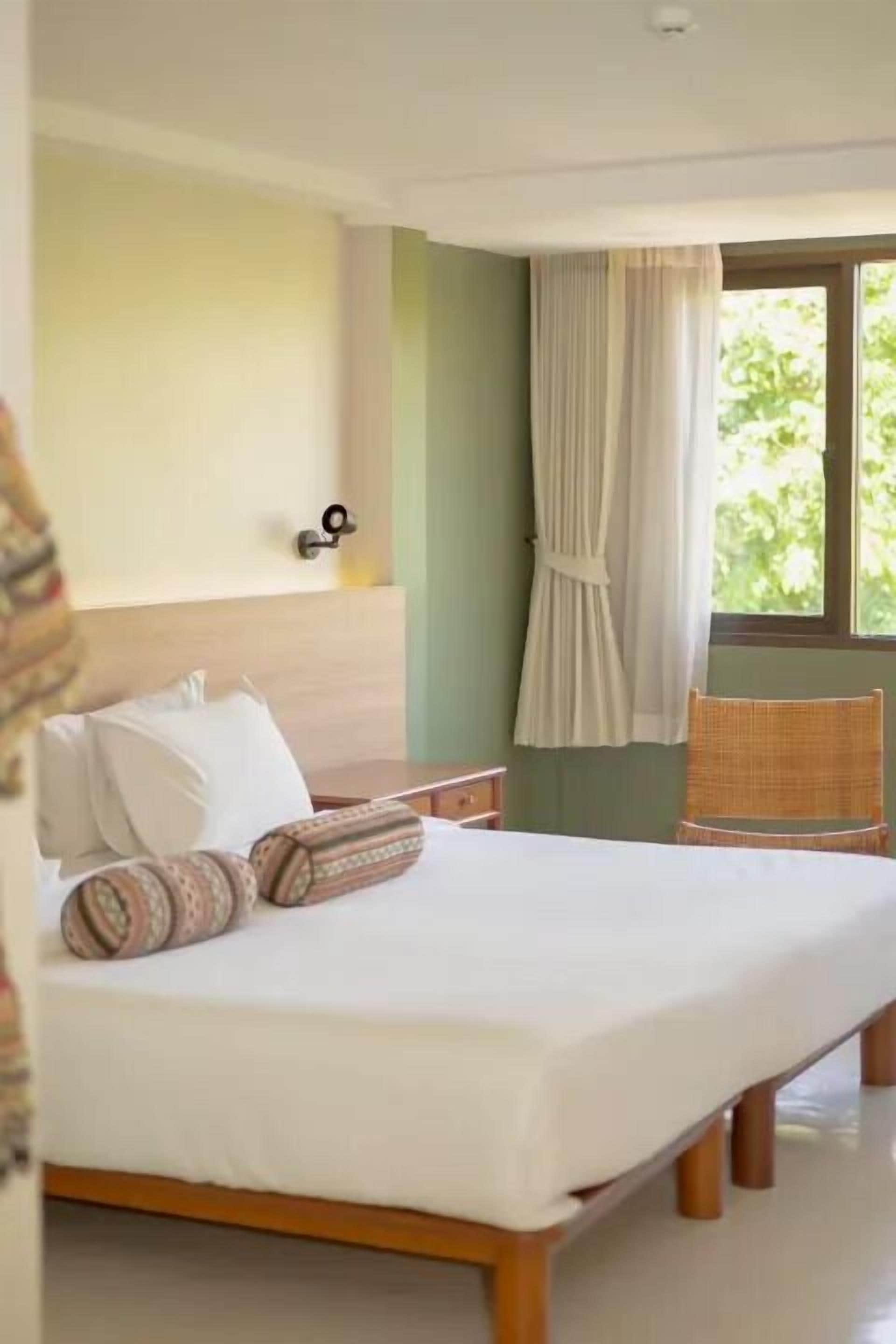 A neatly made bed with patterned pillows, a wooden headboard, and a wicker chair.