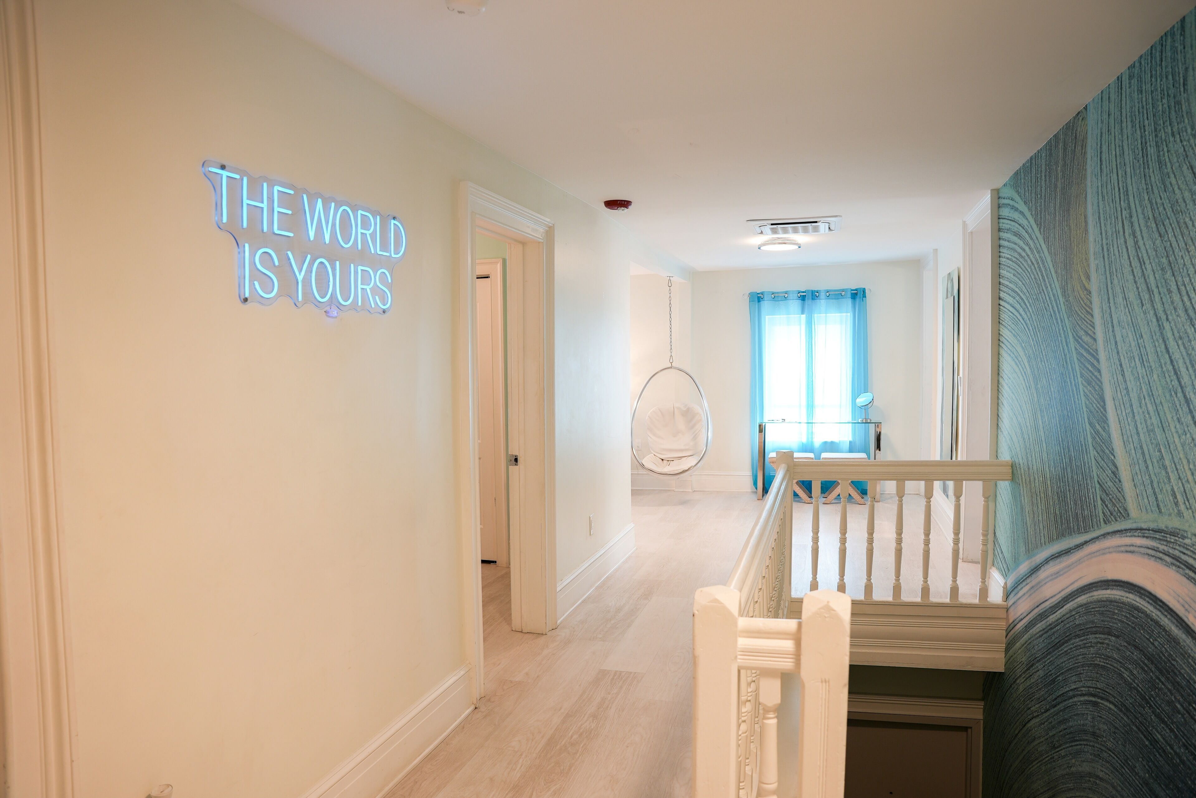 A hallway with a neon sign, a hanging chair, and a staircase.
