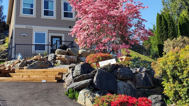 A two-story building with a stone facade, a front porch, and a large pink flowering tree.
