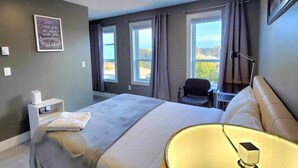 A hotel room with a bed, a desk, a chair, a window with a view, and a bedside lamp.