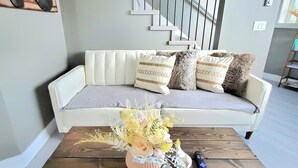 A living room with a white sofa, a wooden coffee table with a vase of flowers, and a clock on the wall.