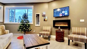 A modern living room with a fireplace, a flat-screen TV mounted on the wall, and a Christmas tree.