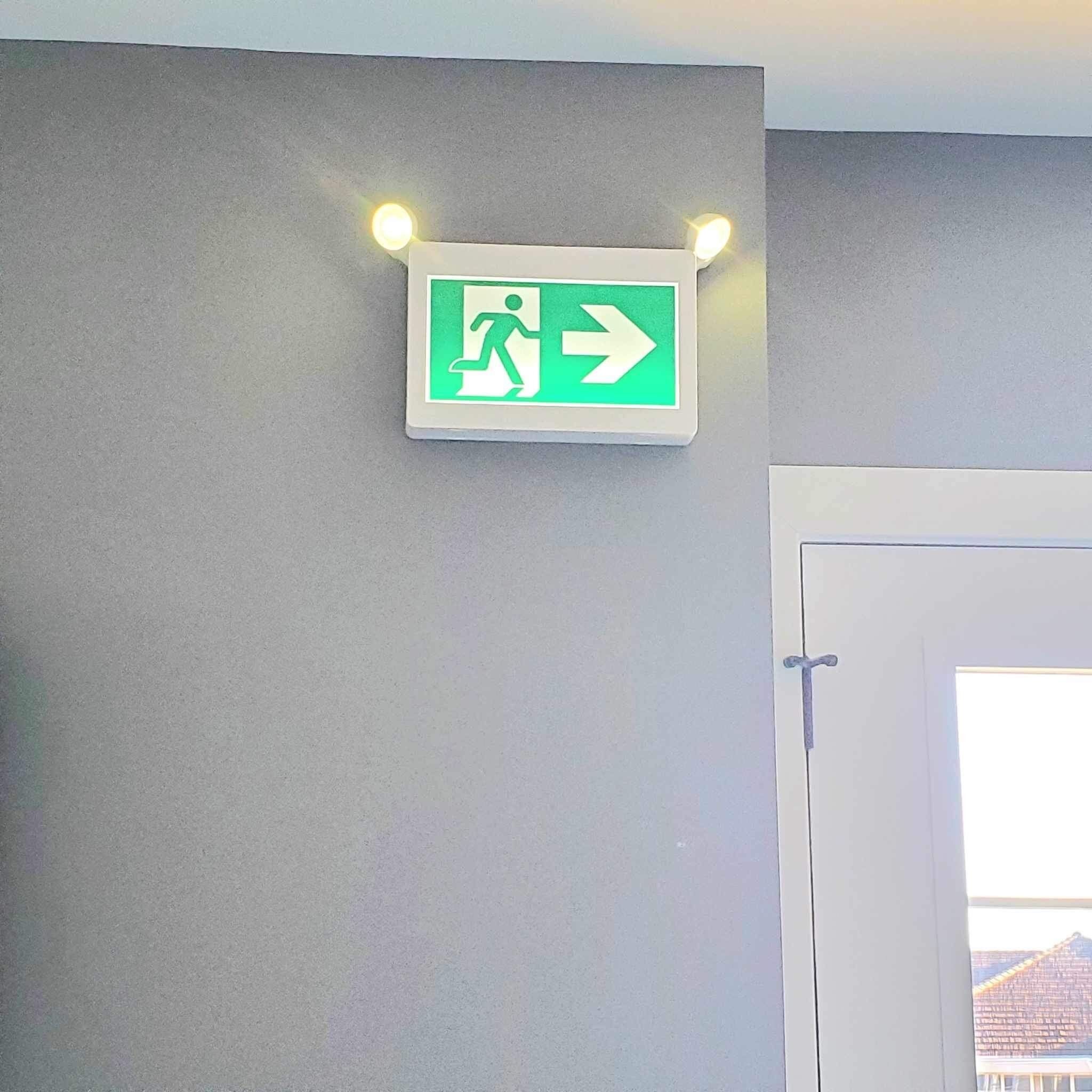 A wall-mounted emergency exit sign with a green arrow and a running figure.