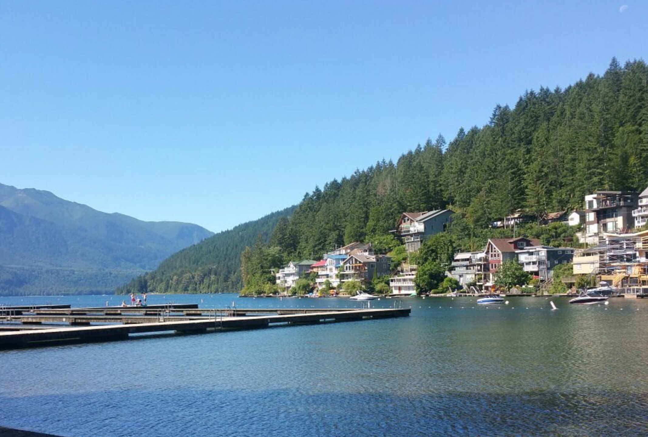 A lakeside town with a dock, houses, and a forested hillside.