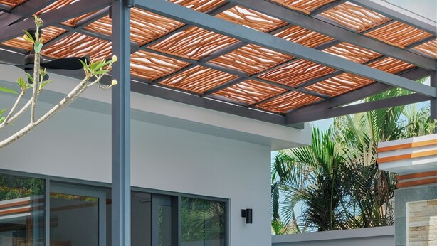A modern outdoor pool area with a curved edge, a covered seating area, and a glass door leading to a room.