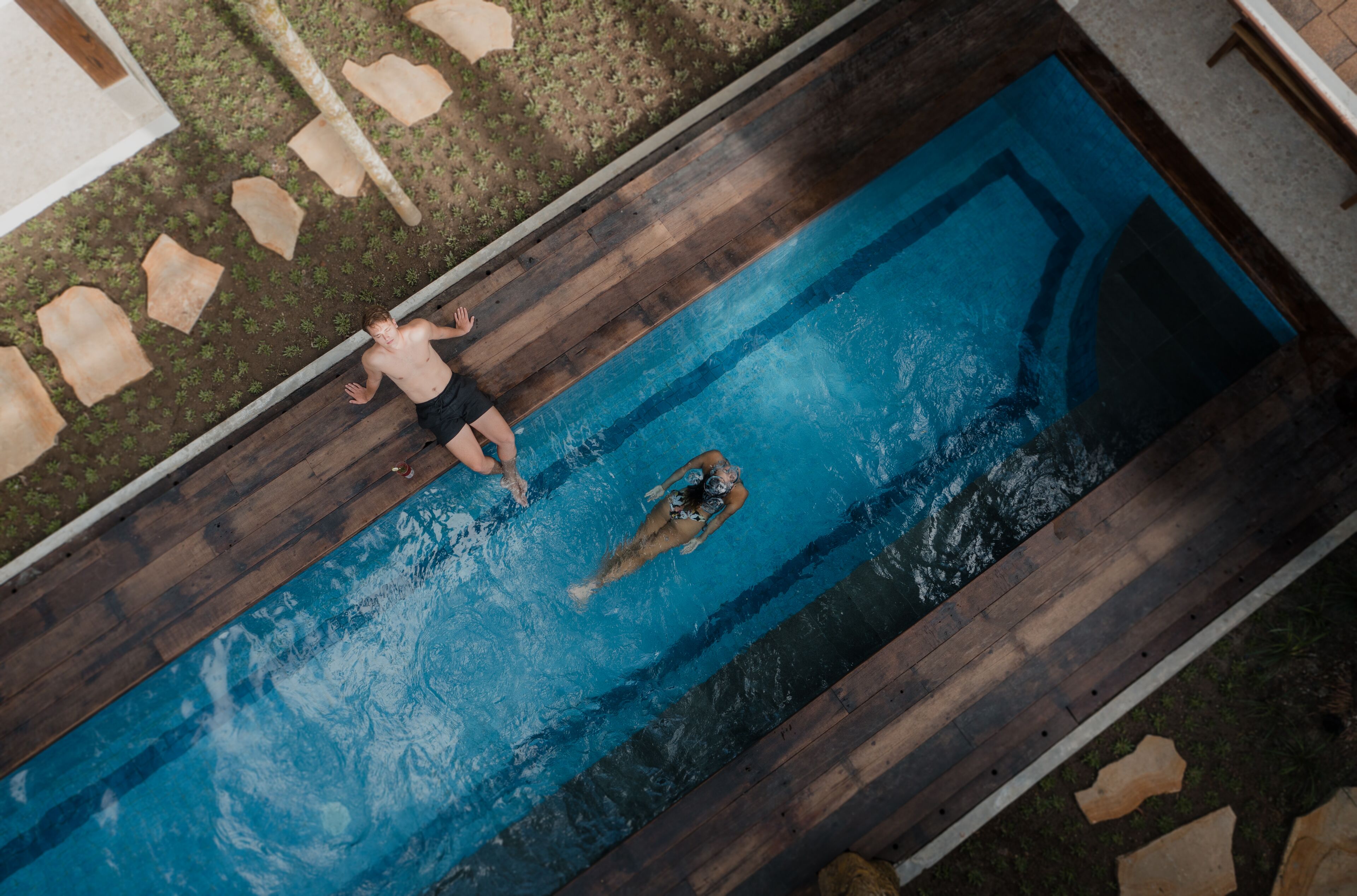 Vue aérienne d’une piscine rectangulaire dotée d’une plage en bois et où une personne nage.