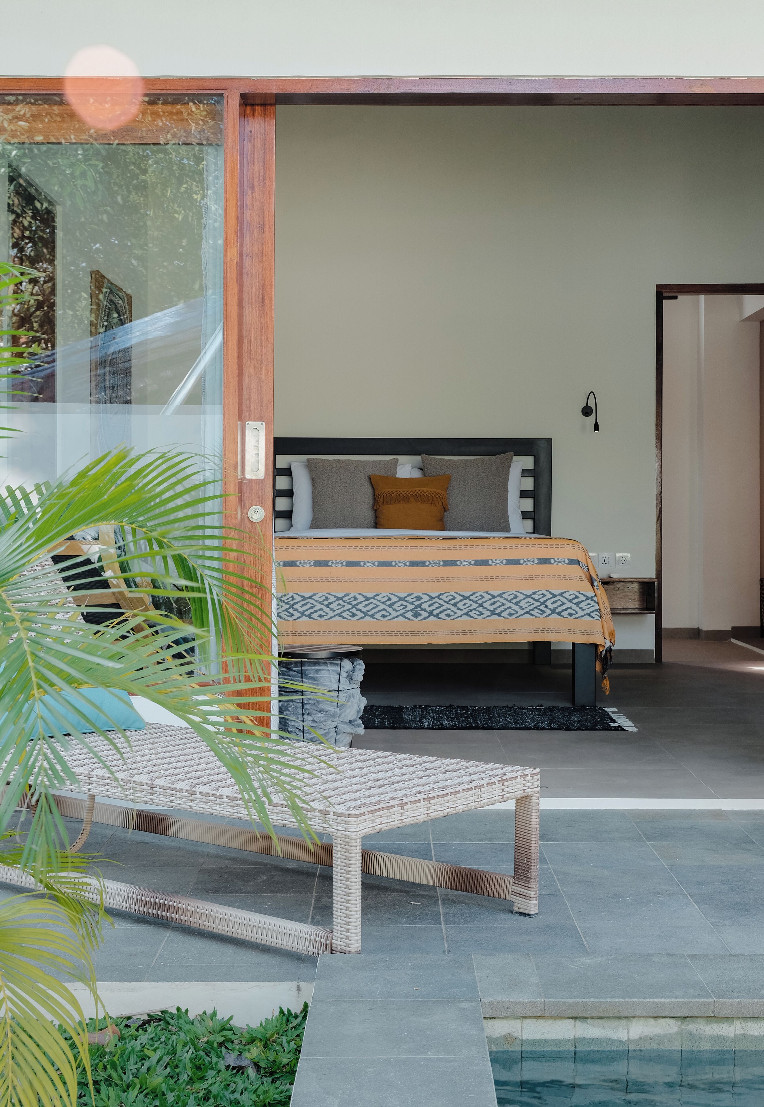 A modern bedroom with a bed, bedside table, and a view of a pool area.