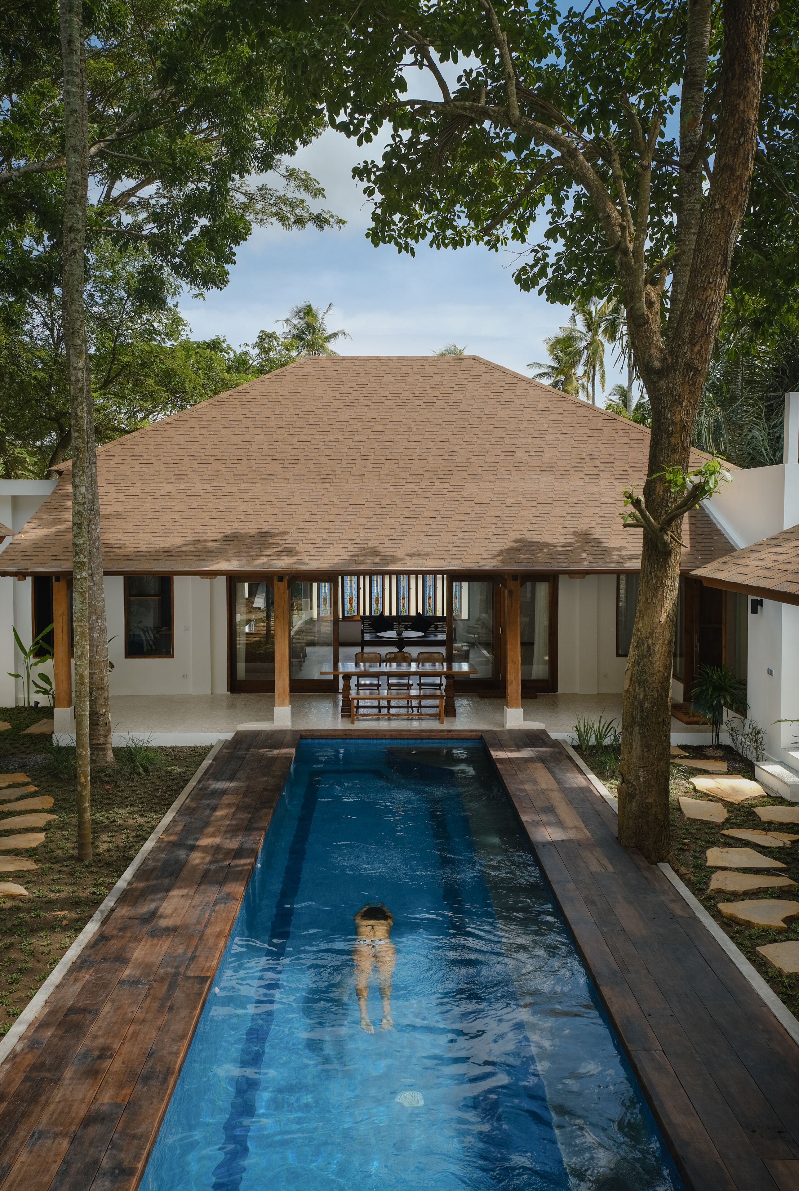 A modern house with a swimming pool, wooden deck, and a dining area with outdoor furniture.