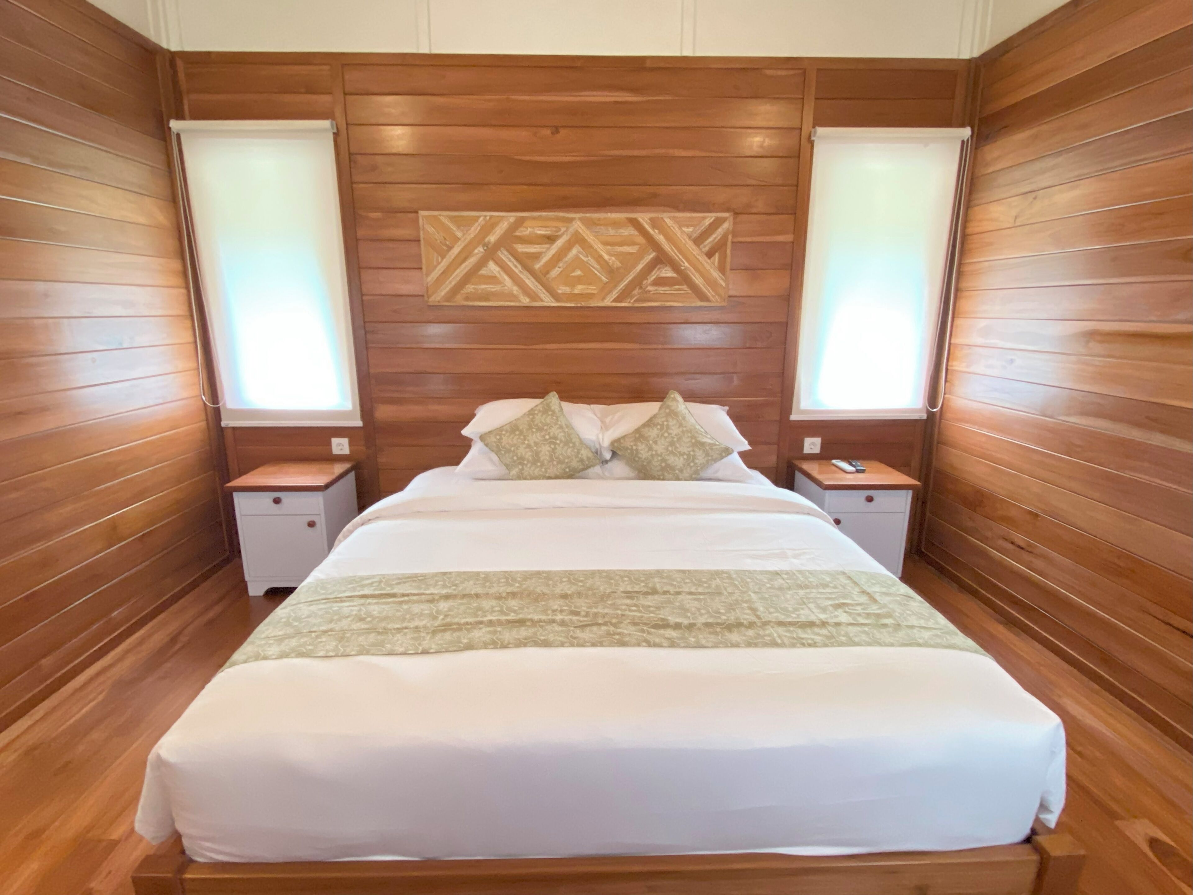 Une chambre avec un grand lit, des lambris en bois sur les murs, deux tables de chevet avec des lampes et un élément décoratif mural au-dessus du lit.