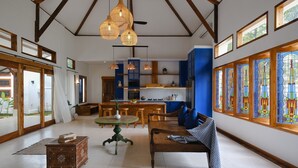 A spacious living area with a wooden bench, a round table, and a kitchen in the background.