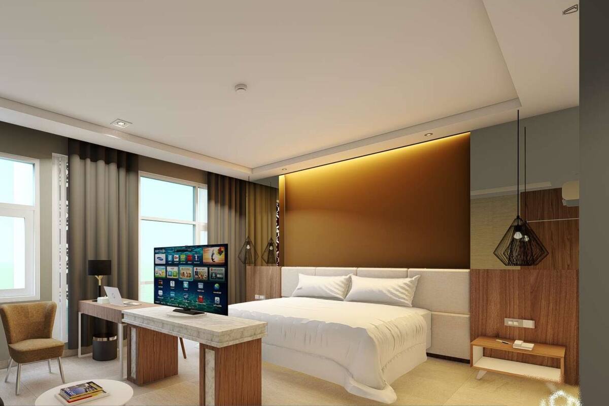 A modern hotel room with a bed, a desk with a laptop, a chair, a TV, and a large window.