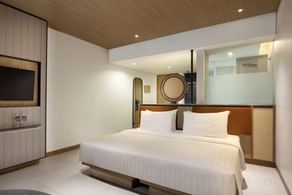 Een moderne hotelkamer met een groot bed, een flatscreen televisie, een spiegel en een klein plankje met toiletartikelen.