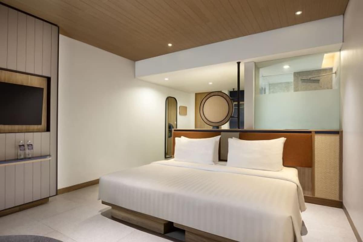 Une chambre d’hôtel moderne avec un grand lit, un téléviseur fixé au mur, un miroir et une tête de lit en bois.