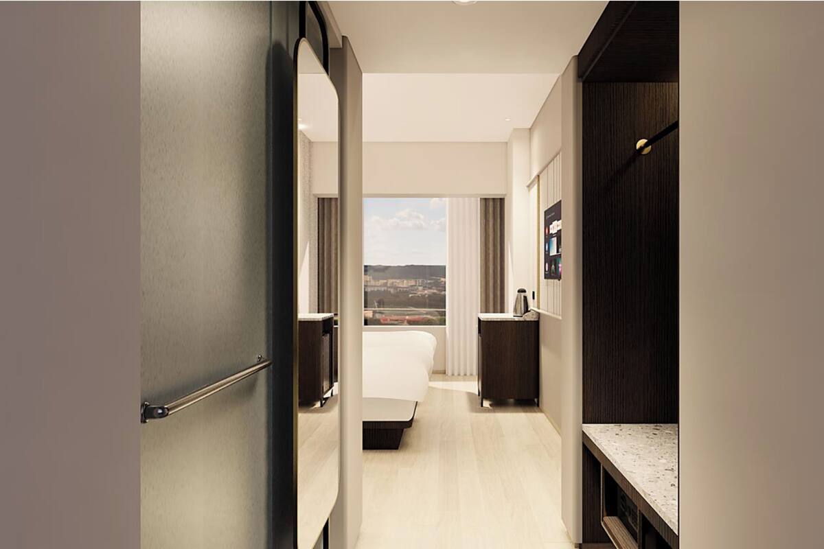 A hotel room with a bed, a desk, a view of the city, and a dark-colored wardrobe.