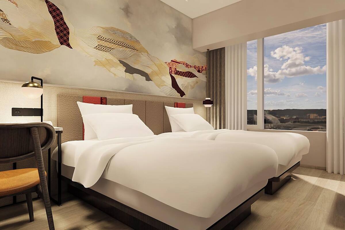 A modern hotel room with a large bed, a desk, and a view of the city through large windows.