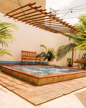 A rectangular hot tub with a wooden bench and a wooden pergola overhead.