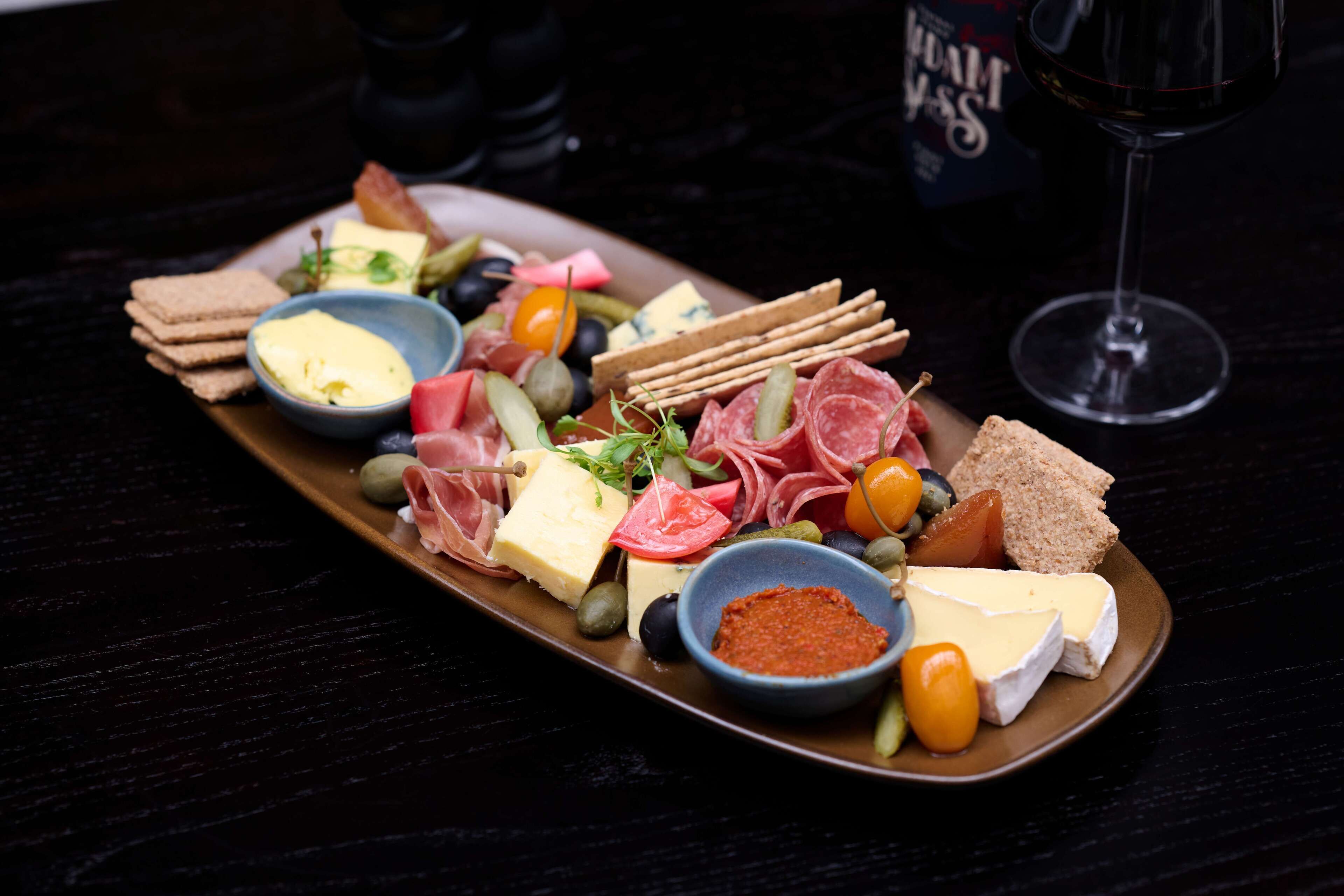 A charcuterie board with various cheeses, meats, olives, and pickles on a wooden table.
