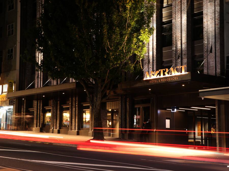 A hotel facade with a large tree in front, illuminated signage, and a modern architectural design.