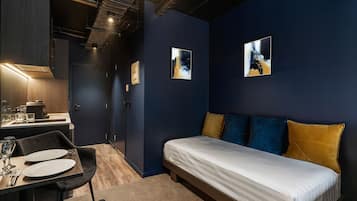 A modern hotel room with a bed, a dining area with a table set for two, and artwork on the walls.