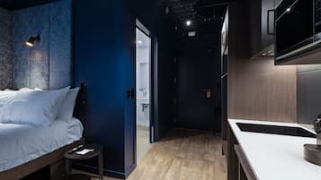 Een moderne hotelkamer met een bed, een klein tafeltje, een kitchenette met een magnetron, en een badkamer die door een open deur zichtbaar is.