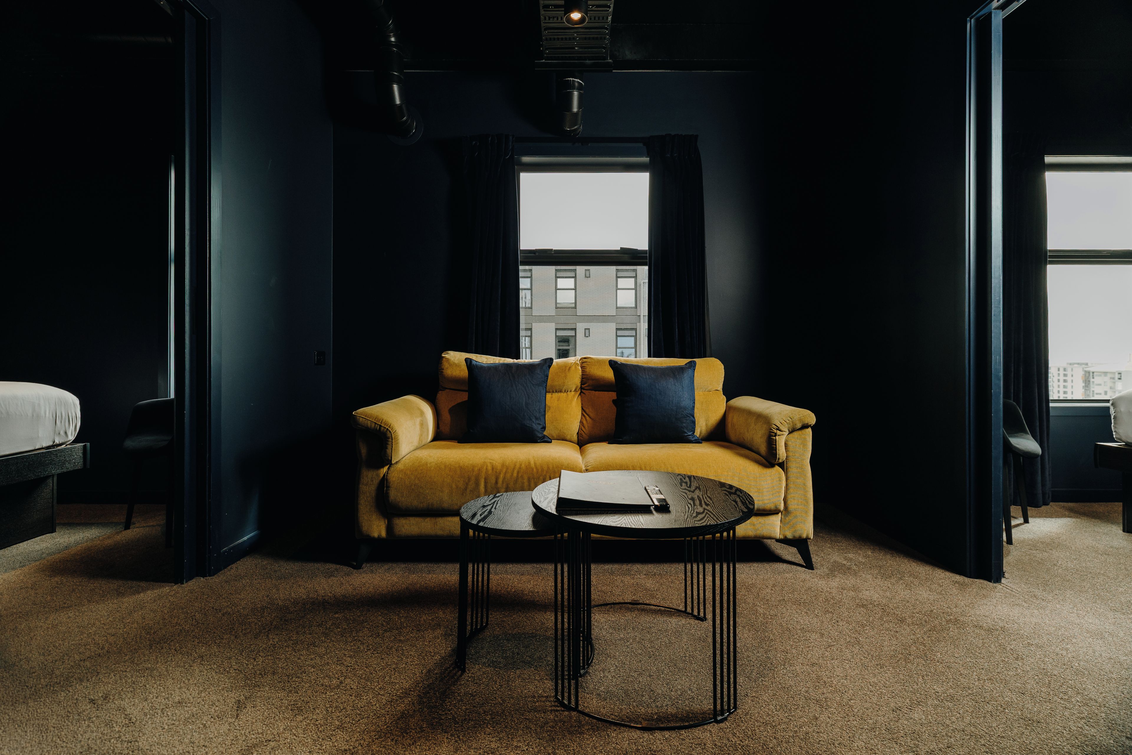 A modern hotel room with a sofa, a coffee table, and a view of the cityscape.