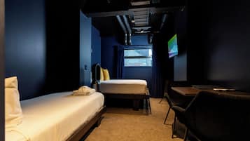 Habitación de hotel con una cama individual, un escritorio, una silla, un televisor y una ventana con vistas a la ciudad.