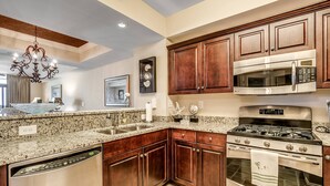 A kitchen with granite countertops, stainless steel appliances, wooden cabinets, and a chandelier.