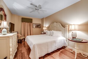 A hotel room with a large bed, a ceiling fan, a dresser, a nightstand, and a table with a lamp.