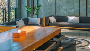 A modern living room with a wooden table, black sofa, and hanging pendant lights. - Villa Konkrete - Tropical 3BR (Kerobokan)
