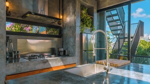 A modern kitchen with a stainless steel range, a built-in oven, and a large window overlooking a cityscape. - Villa Konkrete - Tropical 3BR (Kerobokan)
