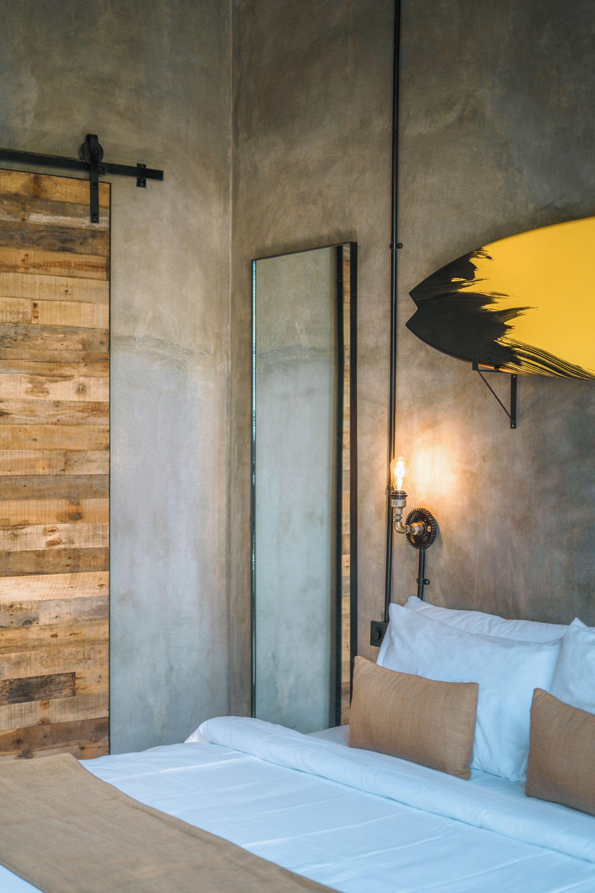 Une chambre avec un panneau mural en bois, un lit avec une literie blanche et marron, un grand miroir et un luminaire fixé au mur.