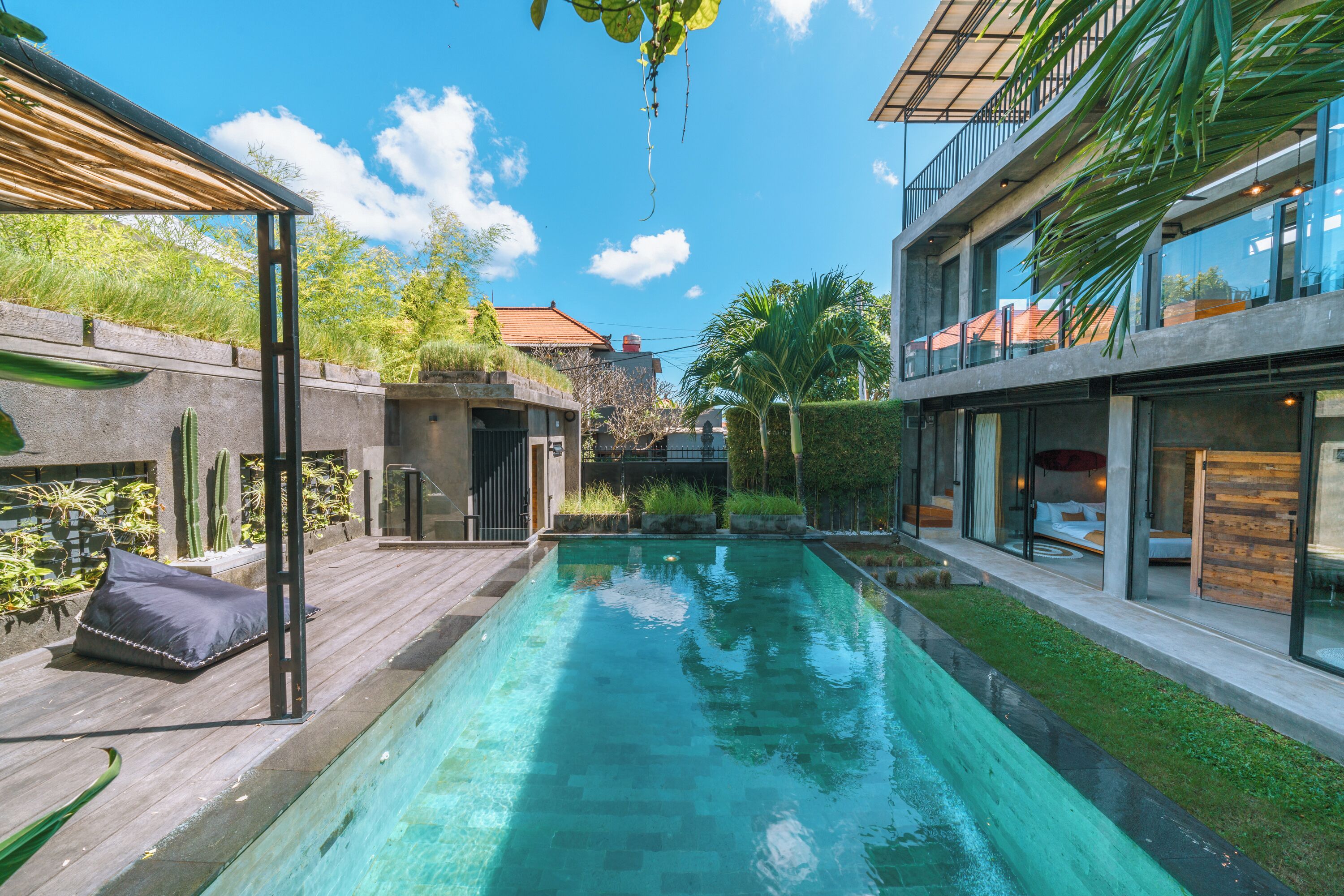 Uma área de piscina moderna ao ar livre, com um deck de madeira, um lounge com paredes de vidro e vista para edifícios próximos.